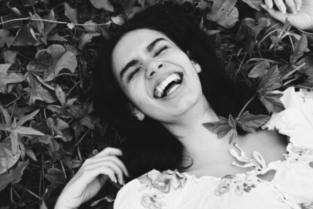 Grayscale Photo of Woman Laughing While Sleeping on Plants