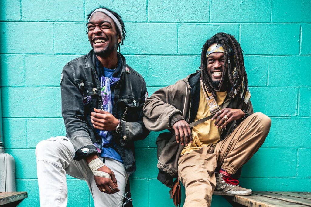 Young African American men with deadlocks in casual clothes in street style standing near green wall